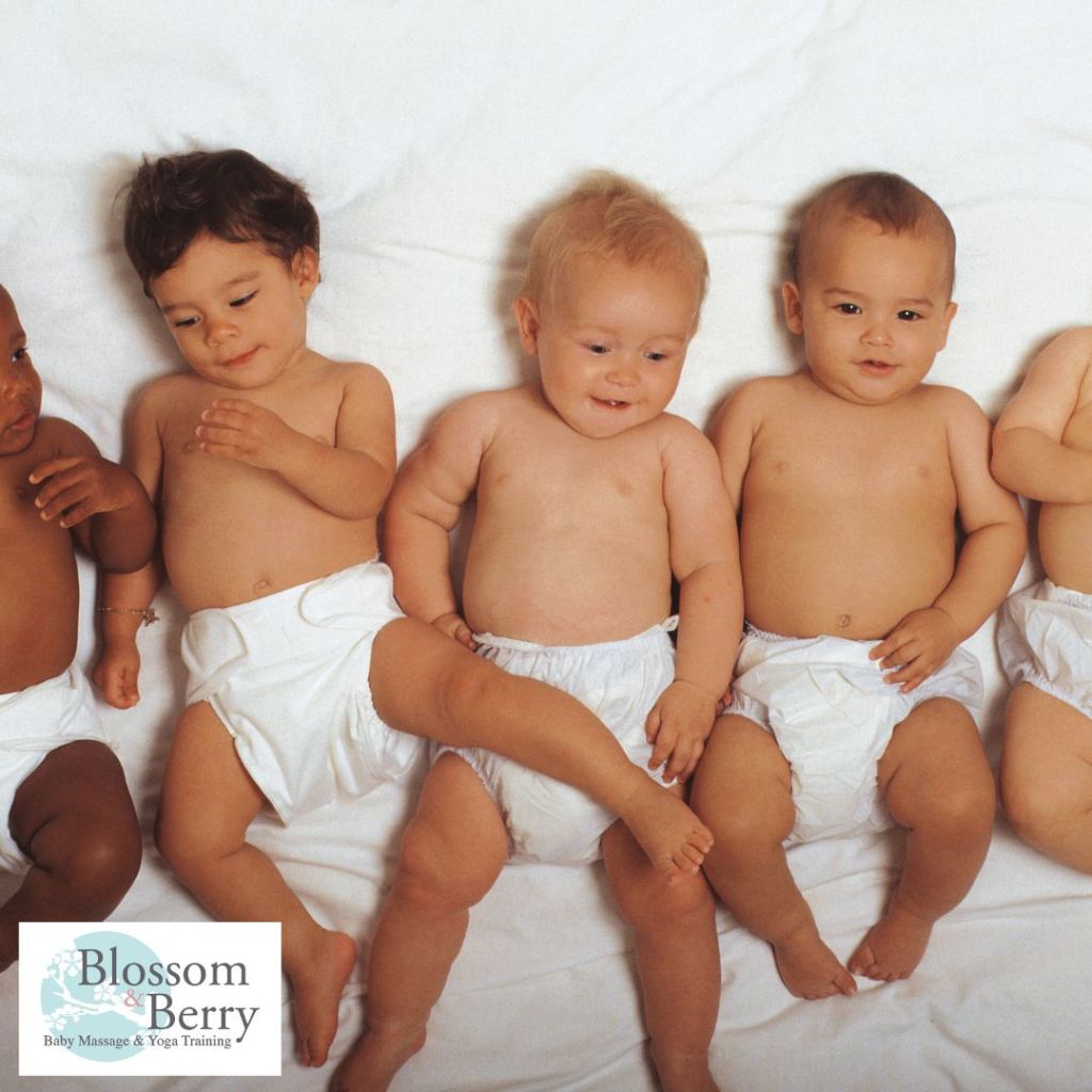 Group of diverse, shirtless babies in cloth diapers resting on a white sheet, with one infant crossing a leg over another, including the 'Blossom & Berry Baby Massage & Yoga Training' logo in the bottom-left corner.